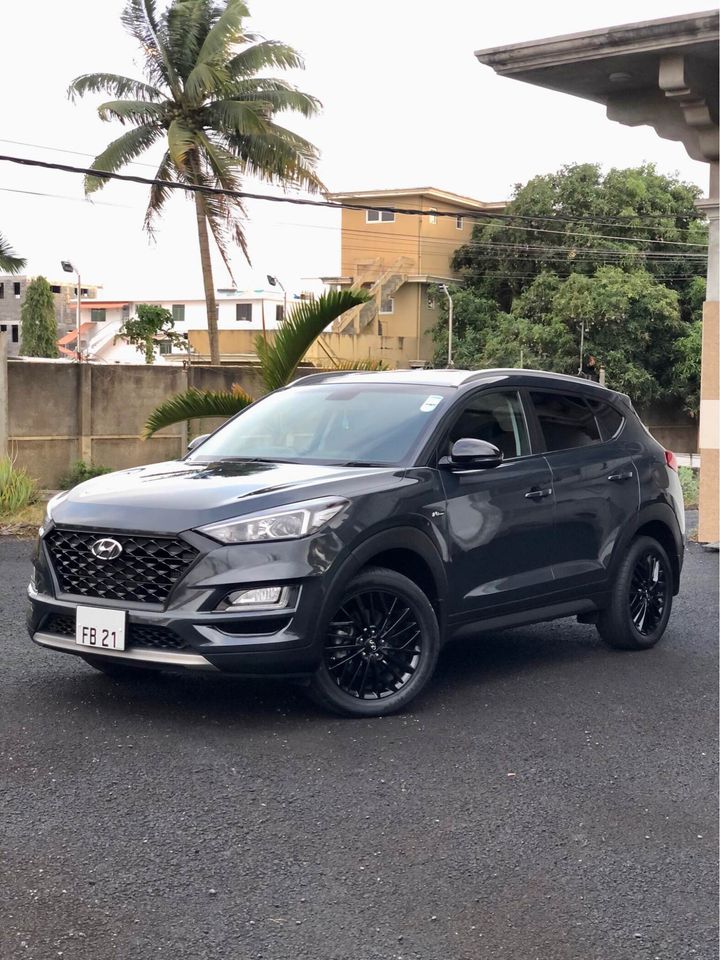 Hyundai Tucson Fury N Line Hybrid SUV from Liberta Car Rental parked at SSR International Airport arrivals, with a chauffeur greeting passengers.