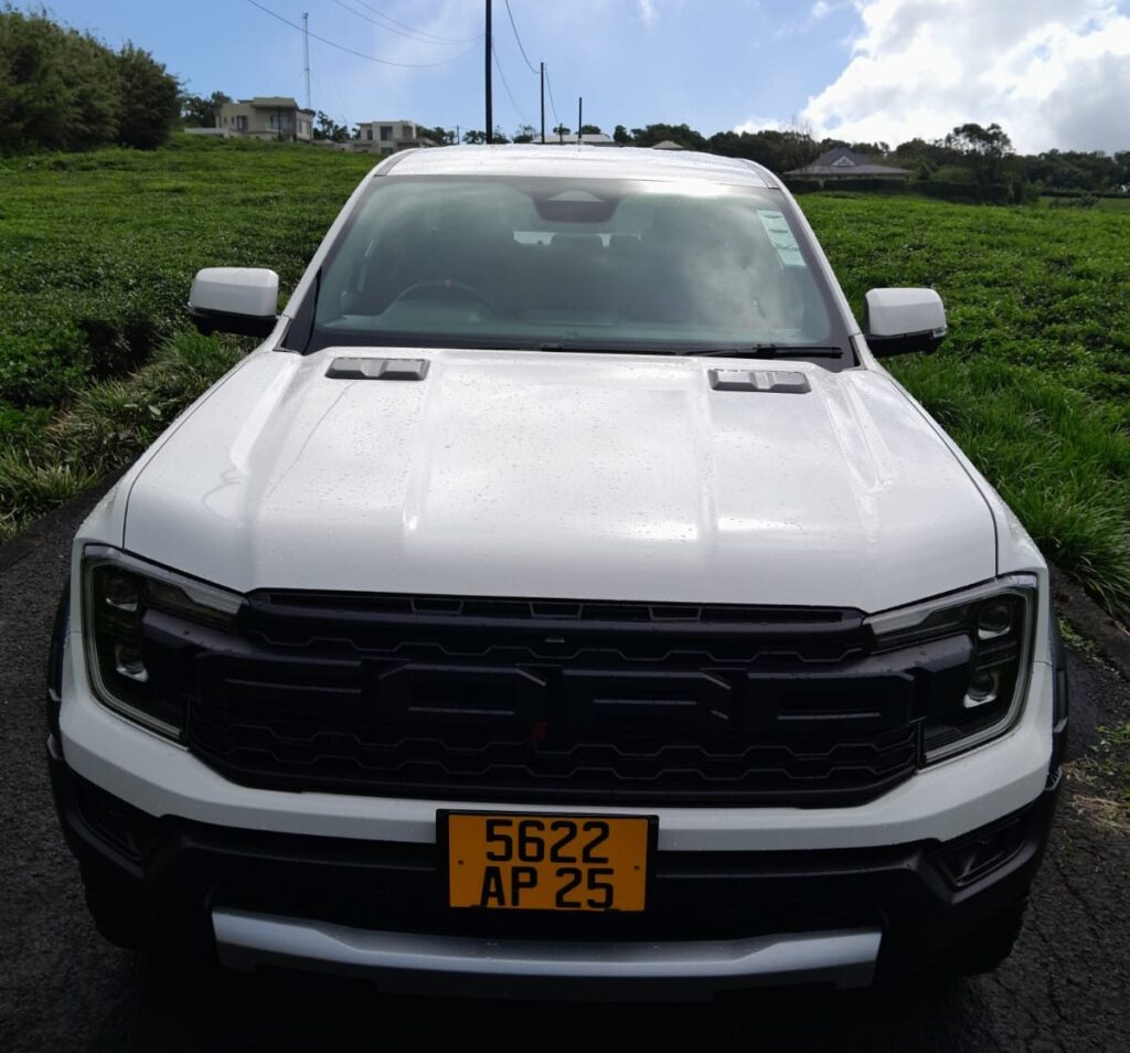 Ford Ranger Raptor 2.0 L Bi-Turbo Diesel rental truck from Liberta Car Rental—matte-blue double-cab splashing through a shallow coastal creek in Mauritius with lush green mountains behind.