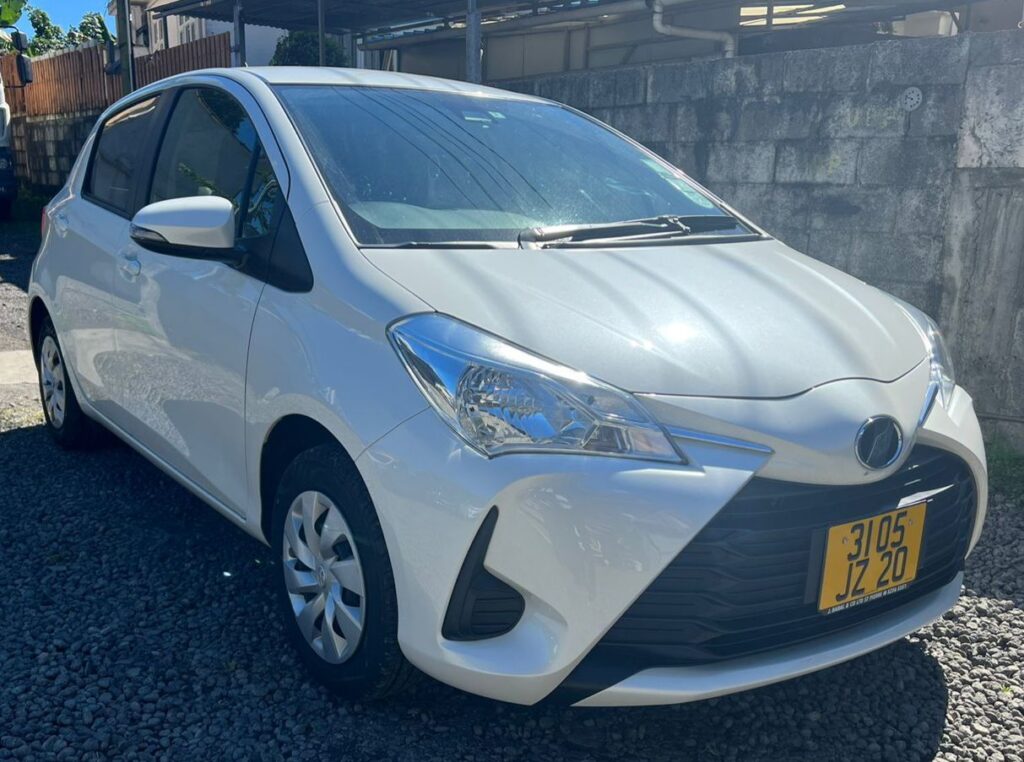 Fuel-efficient Toyota Vitz hatchback from Liberta Car Rental parked beside a turquoise lagoon in Mauritius, with a couple loading snorkeling gear into the boot.