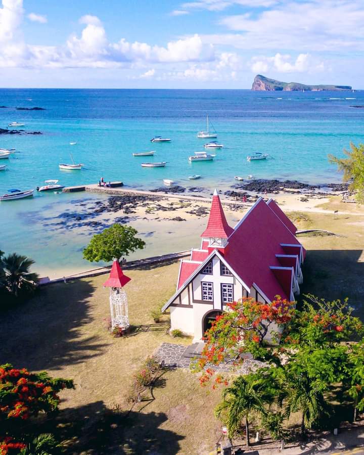 Scenic view of the red-roofed Notre-Dame Auxiliatrice Chapel at Cap Malheureux, Mauritius, with the turquoise ocean in the background.