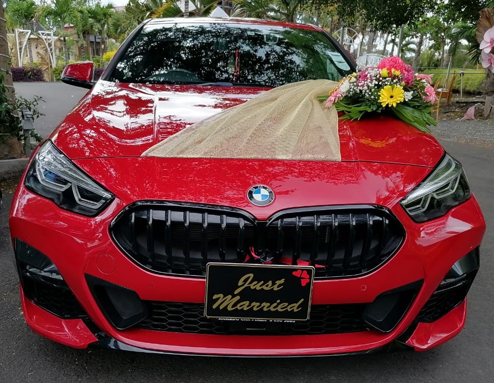 Wedding car rental with driver - Red BMW 218i M Sport with panoramic sunroof parked at a scenic Mauritius wedding venue.