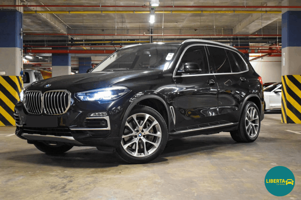 BMW X5 xDrive45e plug-in hybrid from Liberta Car Rental parked outside Mauritius SSR Airport arrivals, with a Liberta agent greeting the driver.