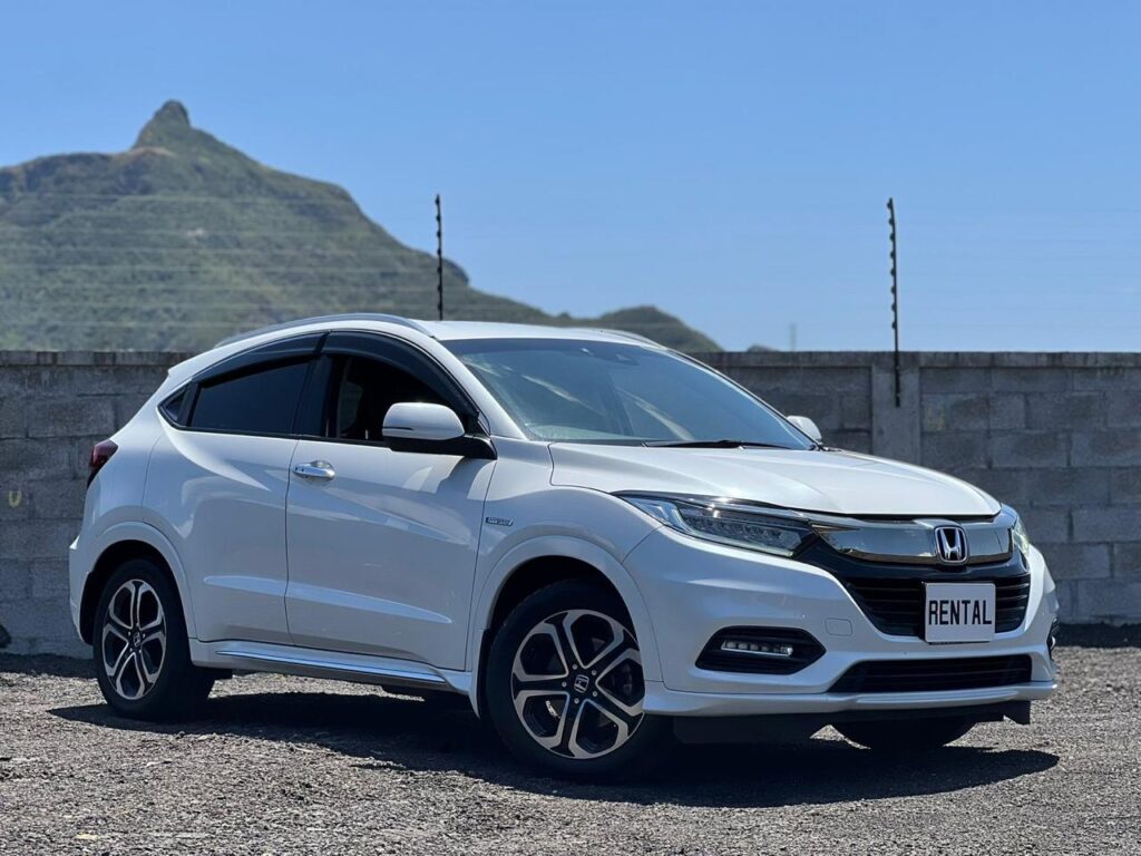 Honda Vezel Hybrid available to rent in Mauritius from Liberta Car Rental—sleek white crossover parked by a turquoise lagoon with palm trees and mountain backdrop.