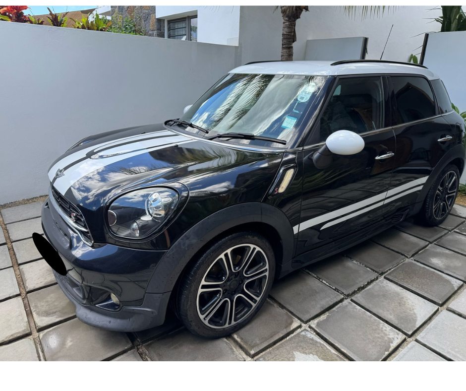 P2P Car Rental Mauritius –Black MINI Cooper Countryman S (manual) navigating a winding coastal road in Mauritius, with turquoise ocean and lush greenery in the background.
